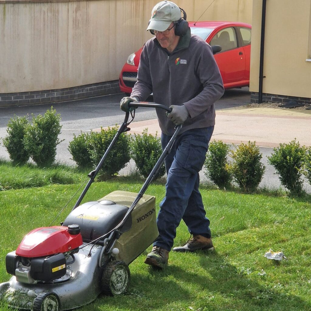 Waterlillie Clark staff member cutting long grass as part of garden maintenance.
